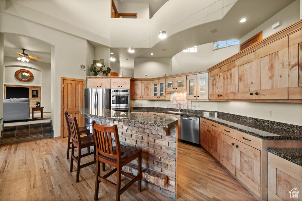 Kitchen featuring stainless steel appliances, a high ceiling, a sink, ceiling fan, and light wood-type flooring