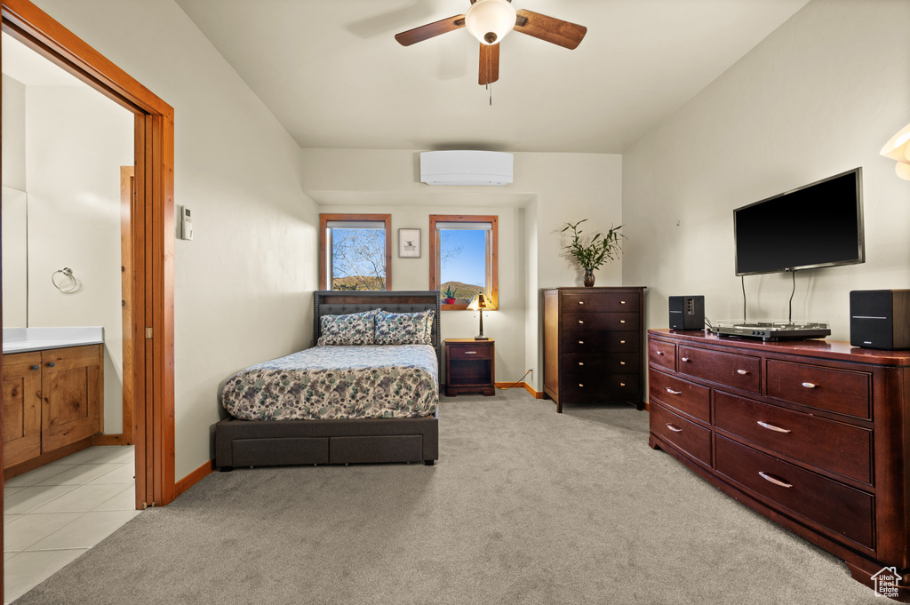Bedroom featuring a wall mounted AC, light colored carpet, baseboards, connected bathroom, and a ceiling fan