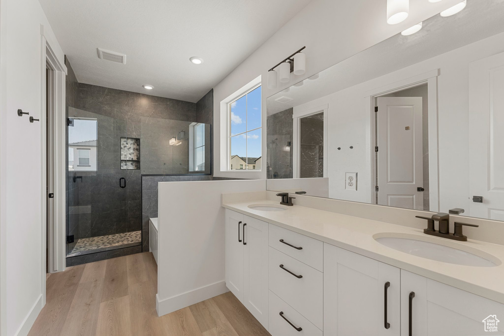 Bathroom featuring a shower stall, wood finished floors, double vanity, recessed lighting, and a tub