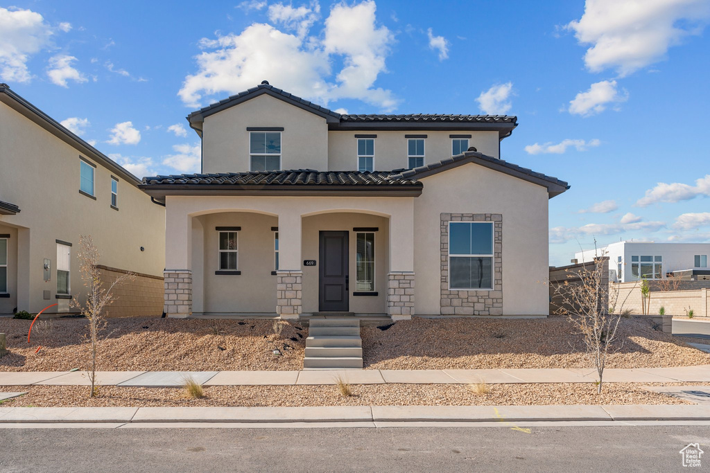 Mediterranean / spanish-style home with stucco siding, a porch, a tiled roof, and stone siding