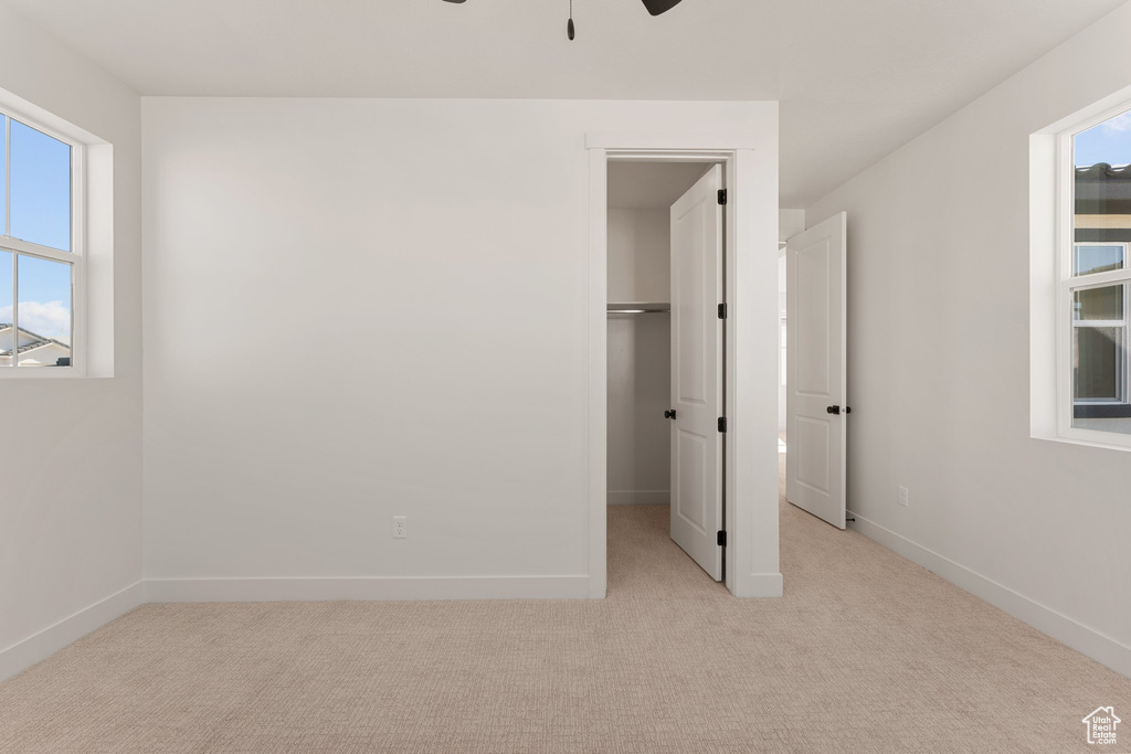 Unfurnished bedroom with a spacious closet, light colored carpet, baseboards, and ceiling fan