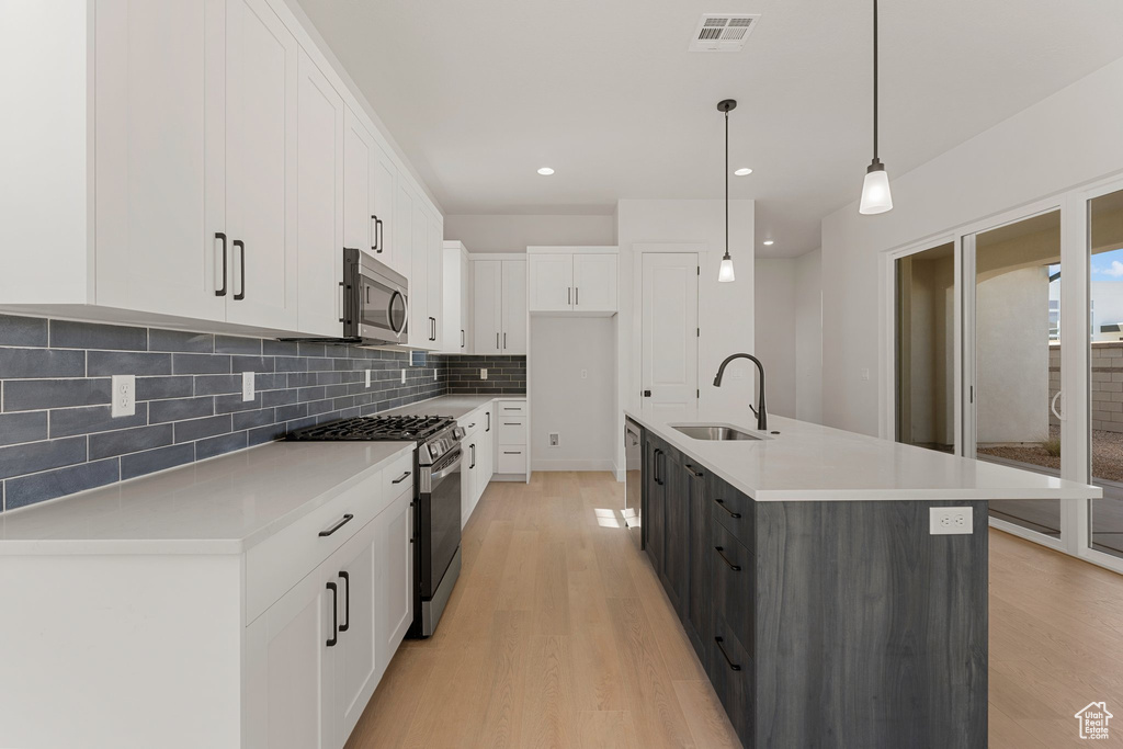 Kitchen featuring appliances with stainless steel finishes, a sink, tasteful backsplash, white cabinetry, and light wood-style flooring