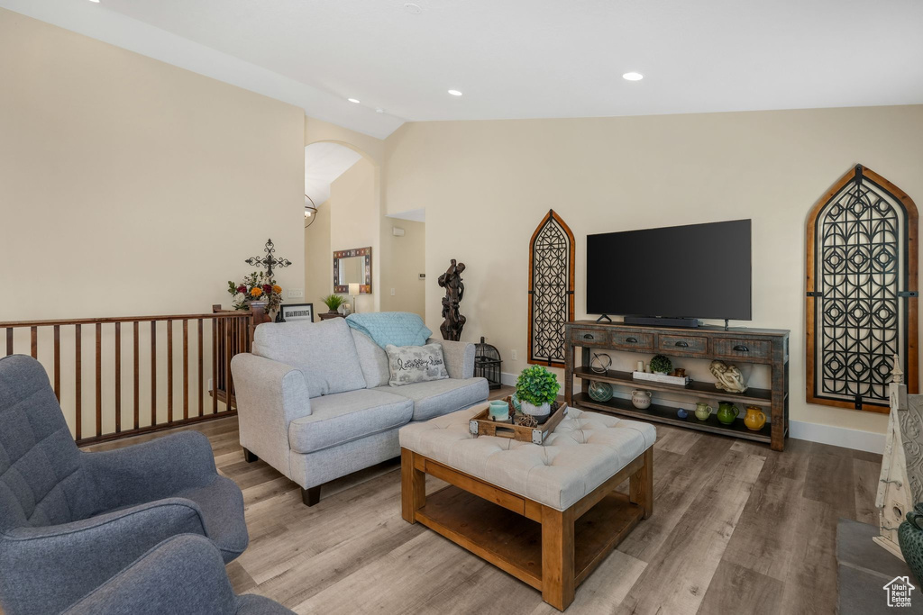 Living room featuring vaulted ceiling, arched walkways, wood finished floors, recessed lighting, and baseboards