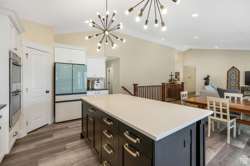 Kitchen with white cabinets, double oven, vaulted ceiling, a chandelier, and light wood-style flooring