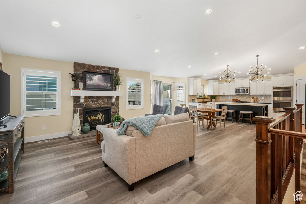 Living room with a chandelier, wood finished floors, a fireplace, recessed lighting, and baseboards