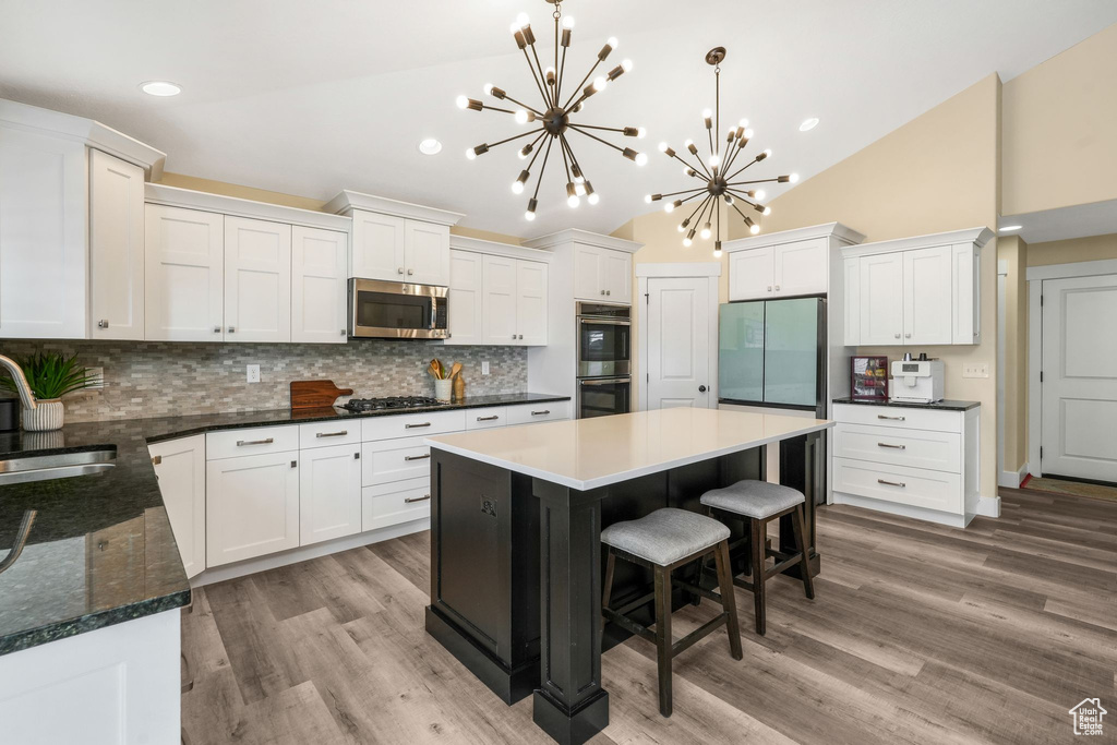 Kitchen featuring appliances with stainless steel finishes, a chandelier, a sink, tasteful backsplash, and white cabinetry
