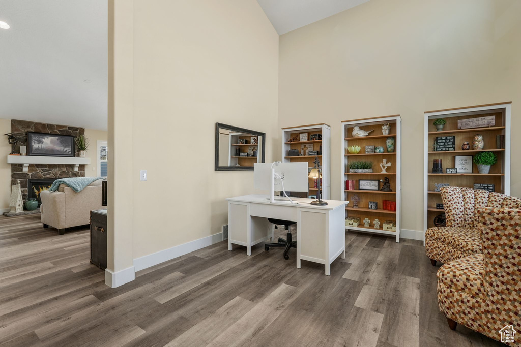 Home office with high vaulted ceiling, dark wood-style flooring, a stone fireplace, and baseboards