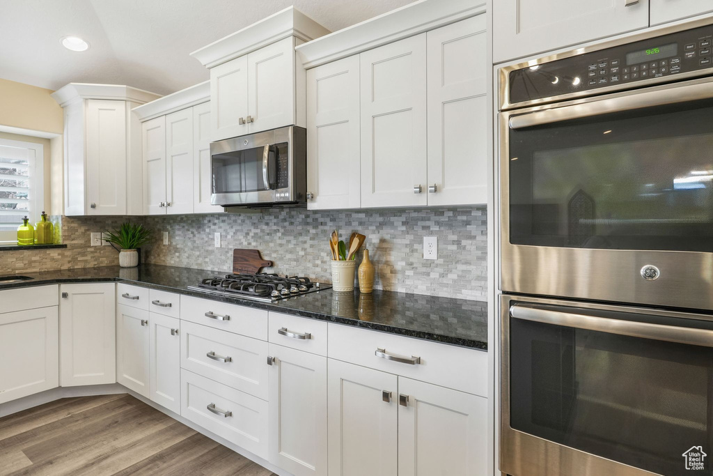 Kitchen featuring stainless steel appliances, backsplash, white cabinetry, light wood finished floors, and recessed lighting