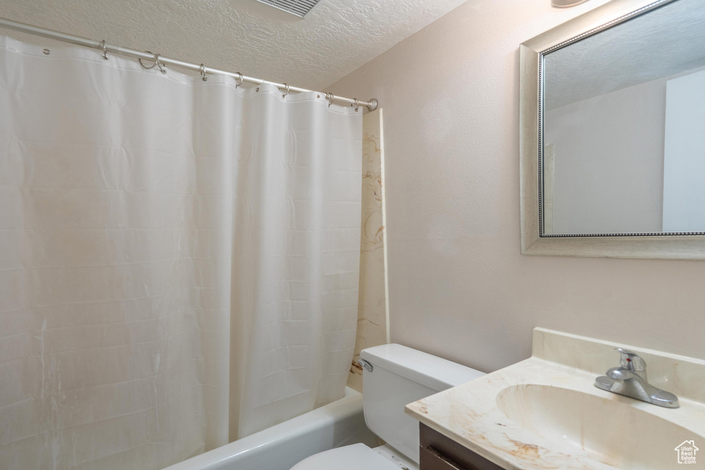 Bathroom with a textured ceiling, vanity, toilet, and shower / bathtub combination with curtain