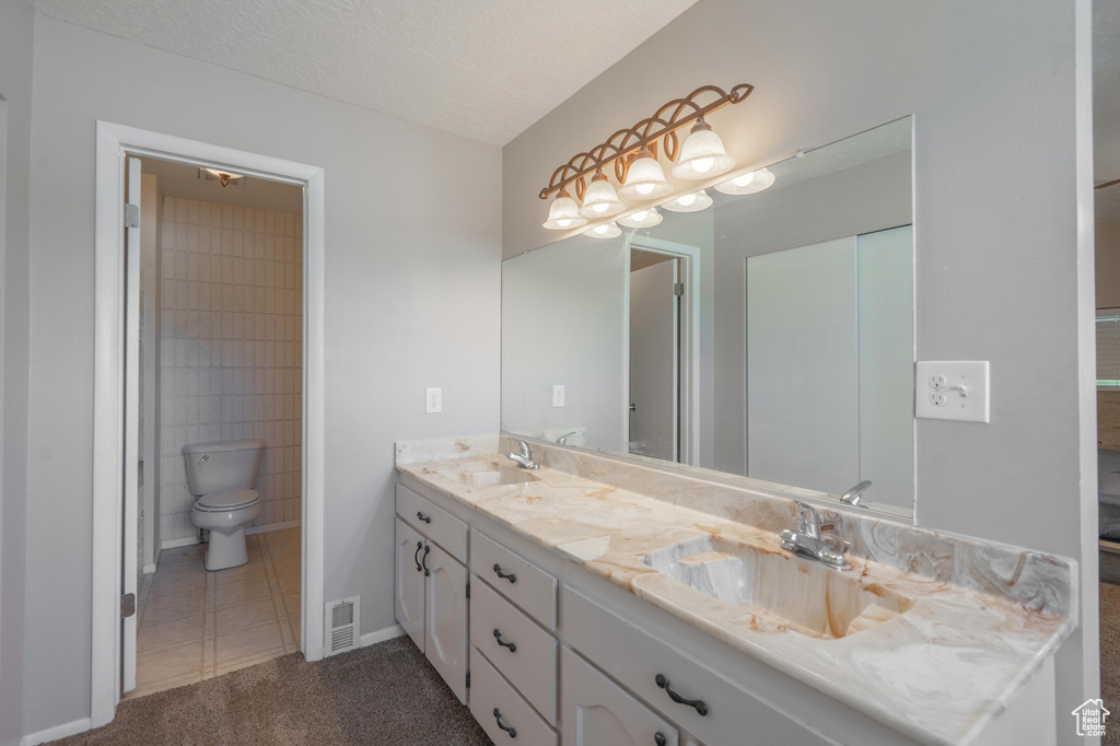 Bathroom with double vanity, tile patterned floors, toilet, and baseboards