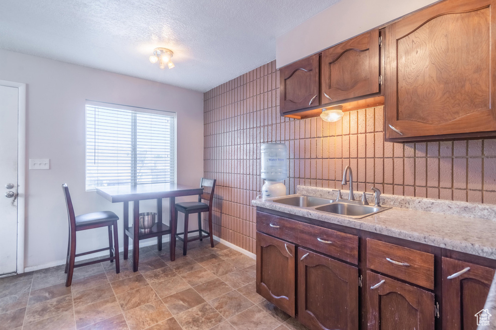 Kitchen with a sink, light countertops, baseboards, decorative backsplash, and a textured ceiling