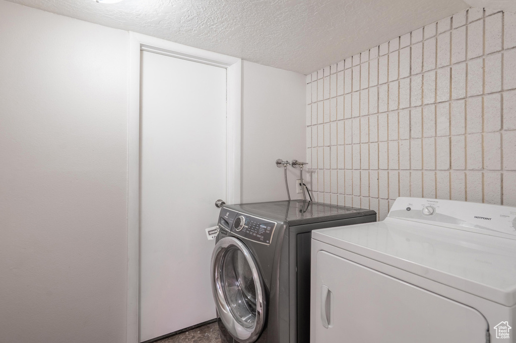 Laundry room with a textured ceiling, washing machine and dryer, and tile walls