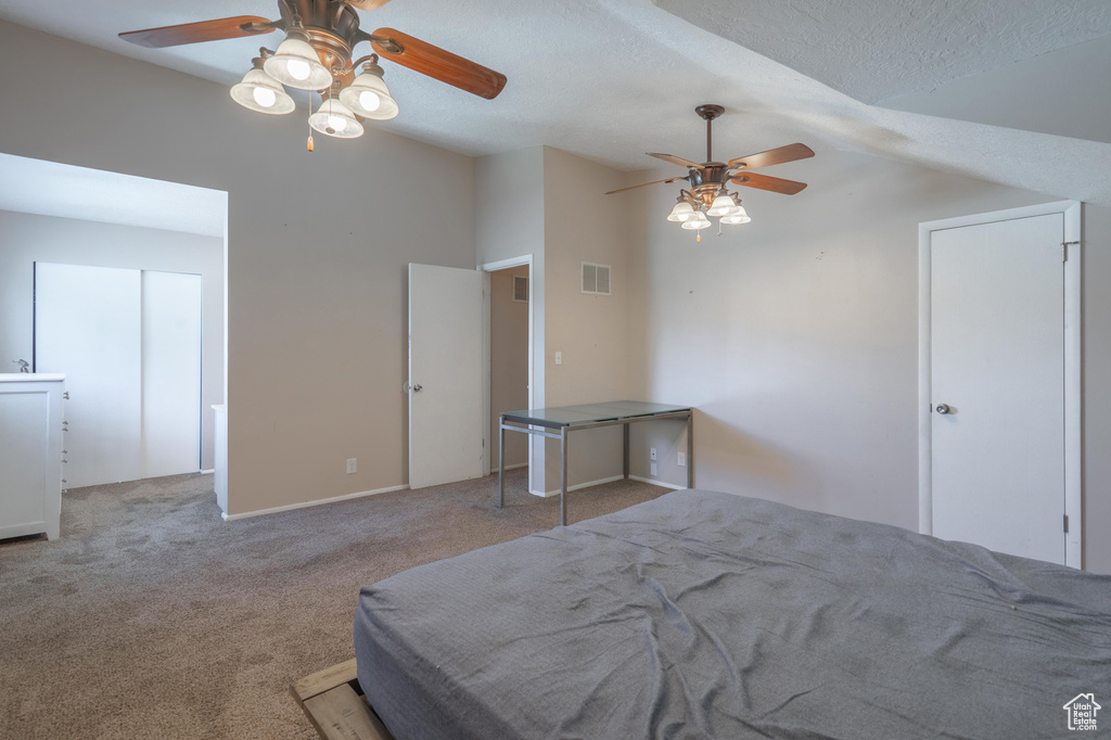 Carpeted bedroom with vaulted ceiling, a textured ceiling, and a ceiling fan