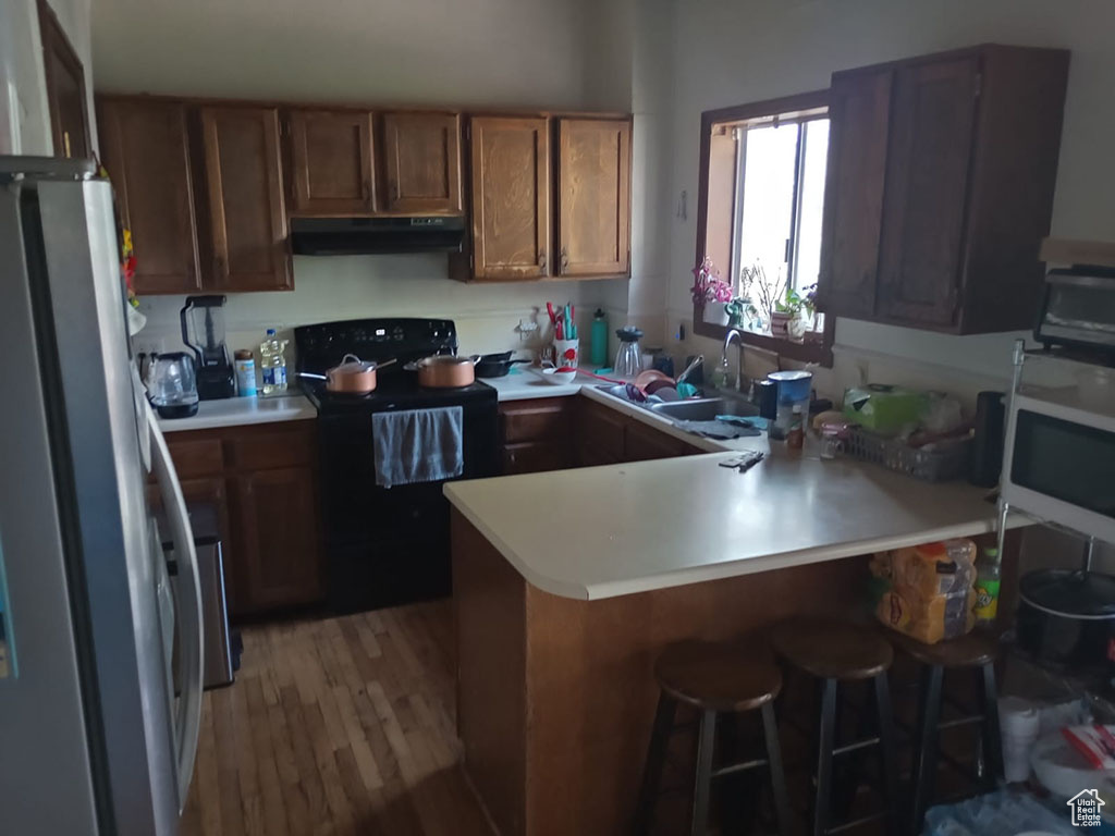 Kitchen featuring black electric range, under cabinet range hood, freestanding refrigerator, white microwave, and a peninsula
