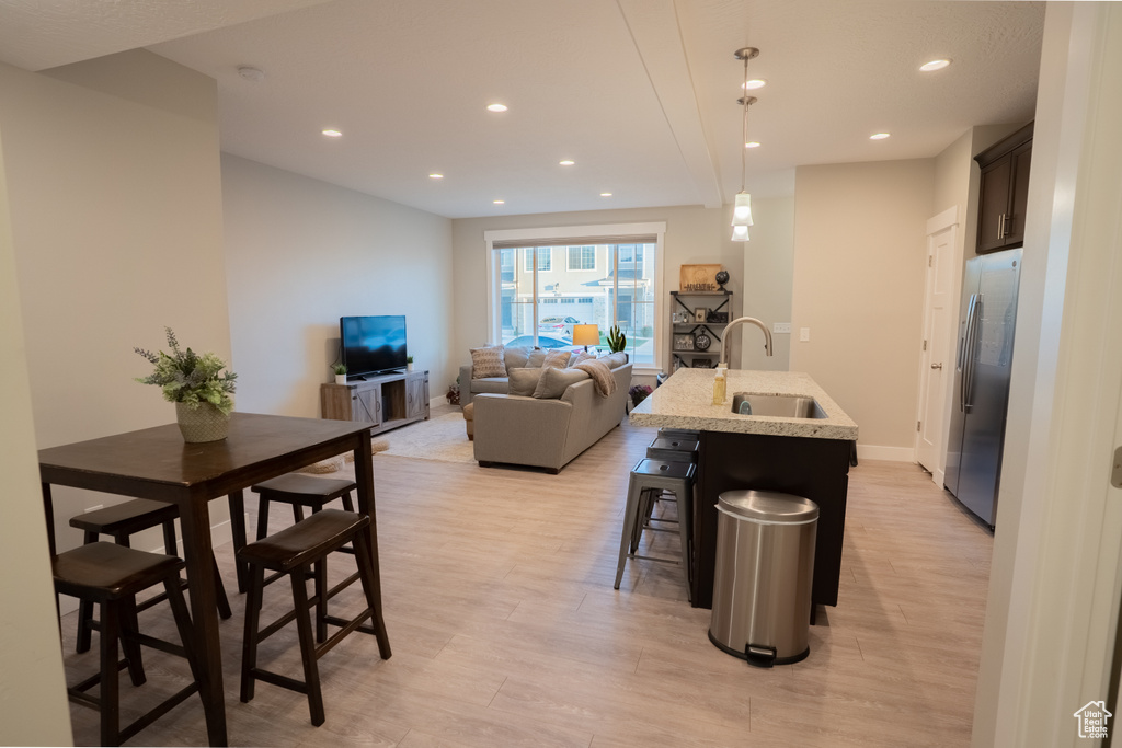 Kitchen with stainless steel fridge, a sink, light wood finished floors, a center island with sink, and recessed lighting