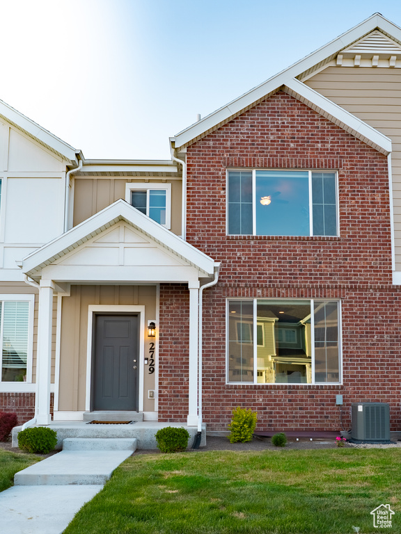 View of front of house featuring central AC unit, brick siding, and a front lawn