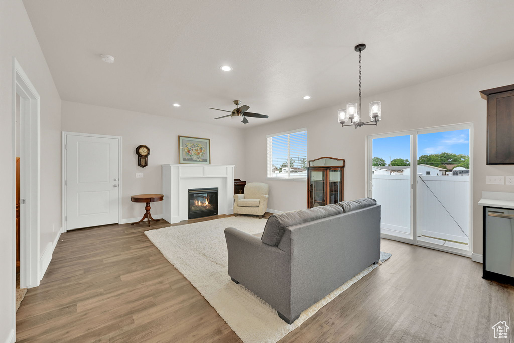 Living area featuring a glass covered fireplace, ceiling fan, wood finished floors, recessed lighting, and a chandelier