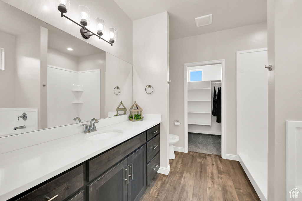 Bathroom featuring wood finished floors, vanity, toilet, a spacious closet, and baseboards