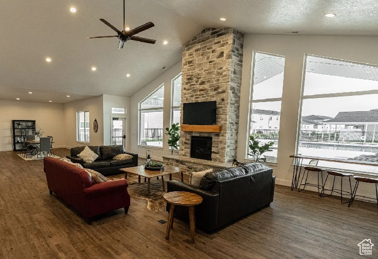 Living area with wood finished floors, ceiling fan, high vaulted ceiling, a stone fireplace, and recessed lighting