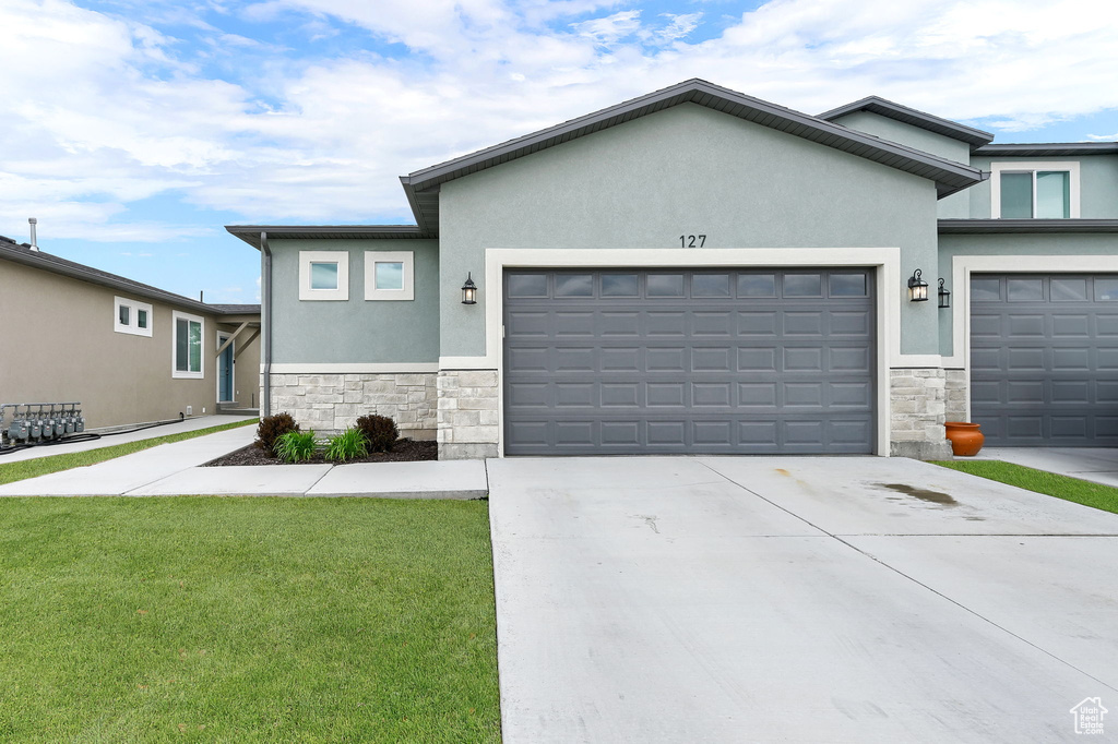 View of front of house featuring stone siding, stucco siding, an attached garage, concrete driveway, and a front yard