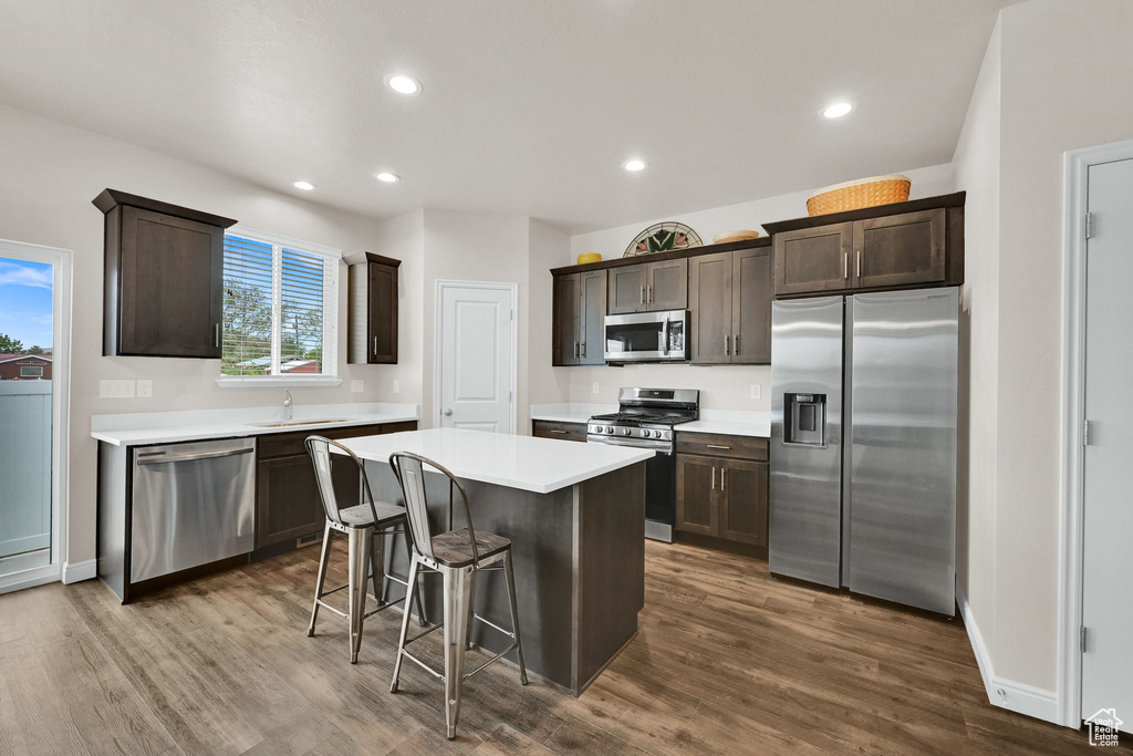 Kitchen with stainless steel appliances, a center island, dark brown cabinetry, dark wood-style floors, and light countertops