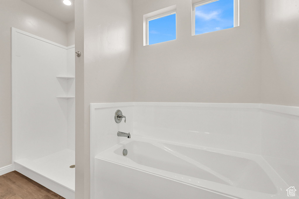 Full bathroom featuring walk in shower, wood finished floors, a bath, and baseboards