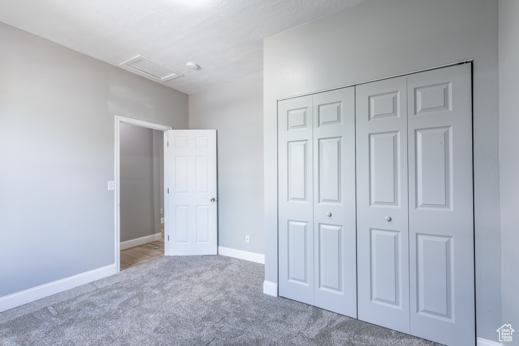 Unfurnished bedroom with attic access, carpet flooring, a closet, and baseboards