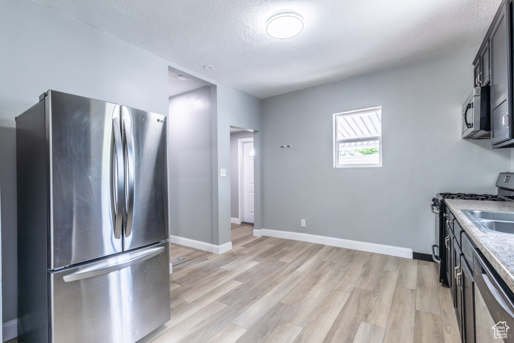 Kitchen with appliances with stainless steel finishes, light wood-style flooring, a textured ceiling, light countertops, and baseboards