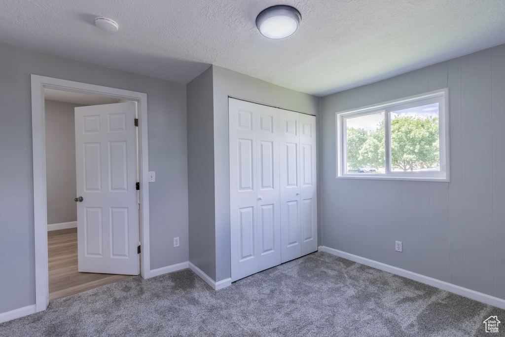Unfurnished bedroom featuring carpet floors, a closet, a textured ceiling, and baseboards