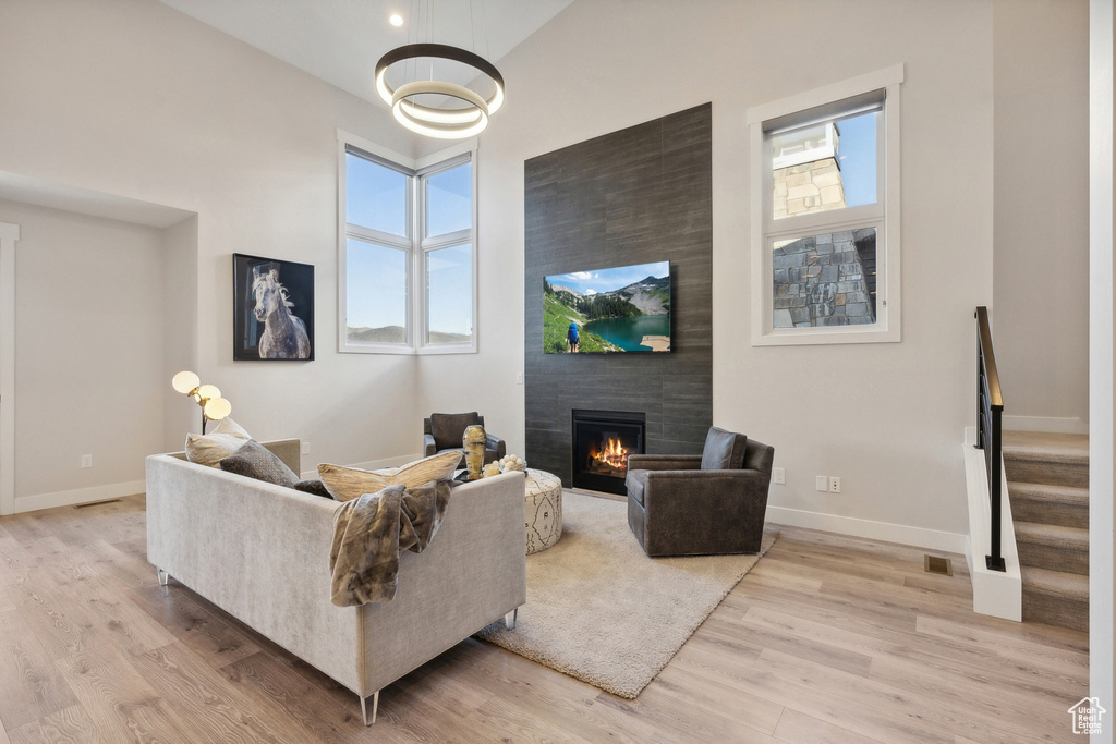 Living area featuring a fireplace, light wood-type flooring, baseboards, a towering ceiling, and stairs