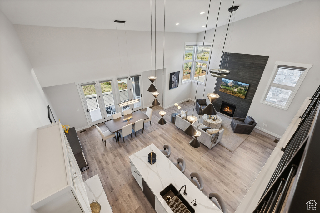 Living room with light wood-style flooring, baseboards, recessed lighting, a towering ceiling, and a warm lit fireplace