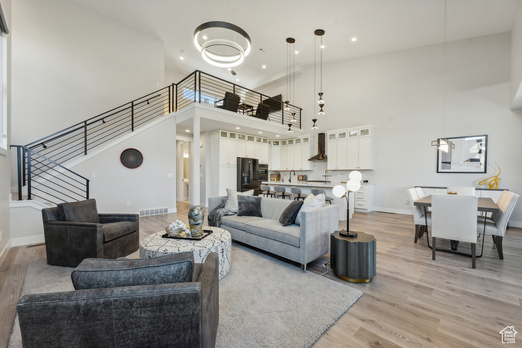 Living area with light wood finished floors, stairs, a towering ceiling, baseboards, and recessed lighting