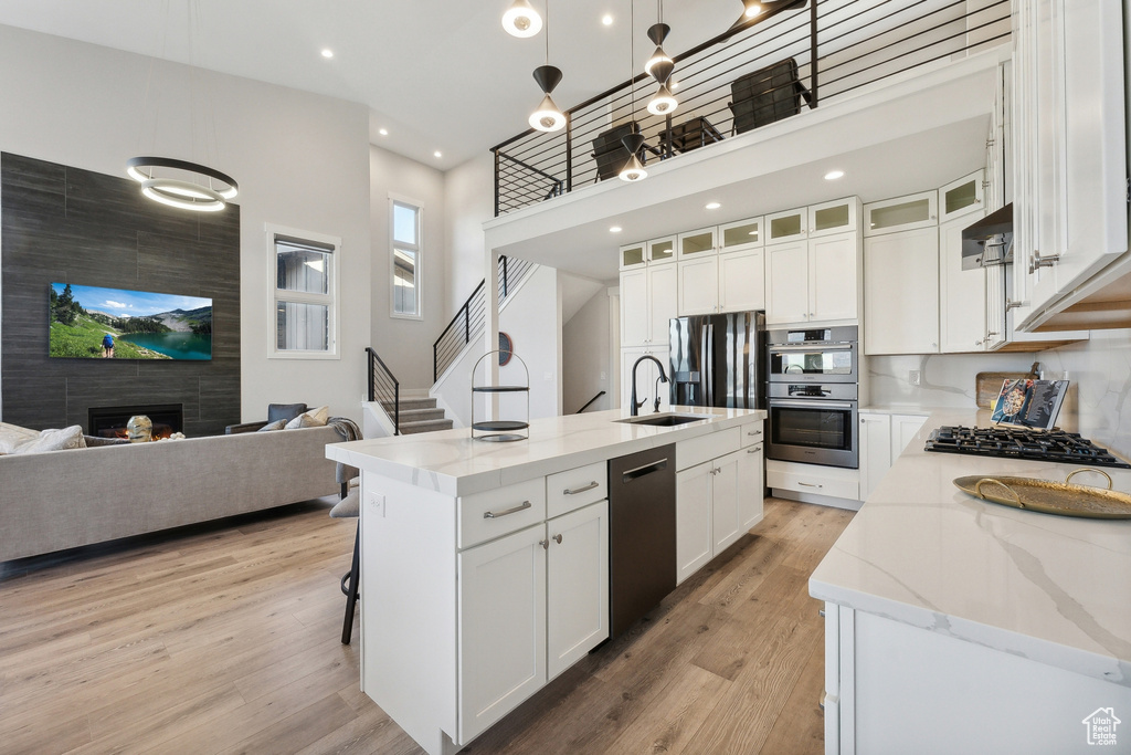 Kitchen with stainless steel appliances, a sink, white cabinetry, light stone counters, and light wood finished floors