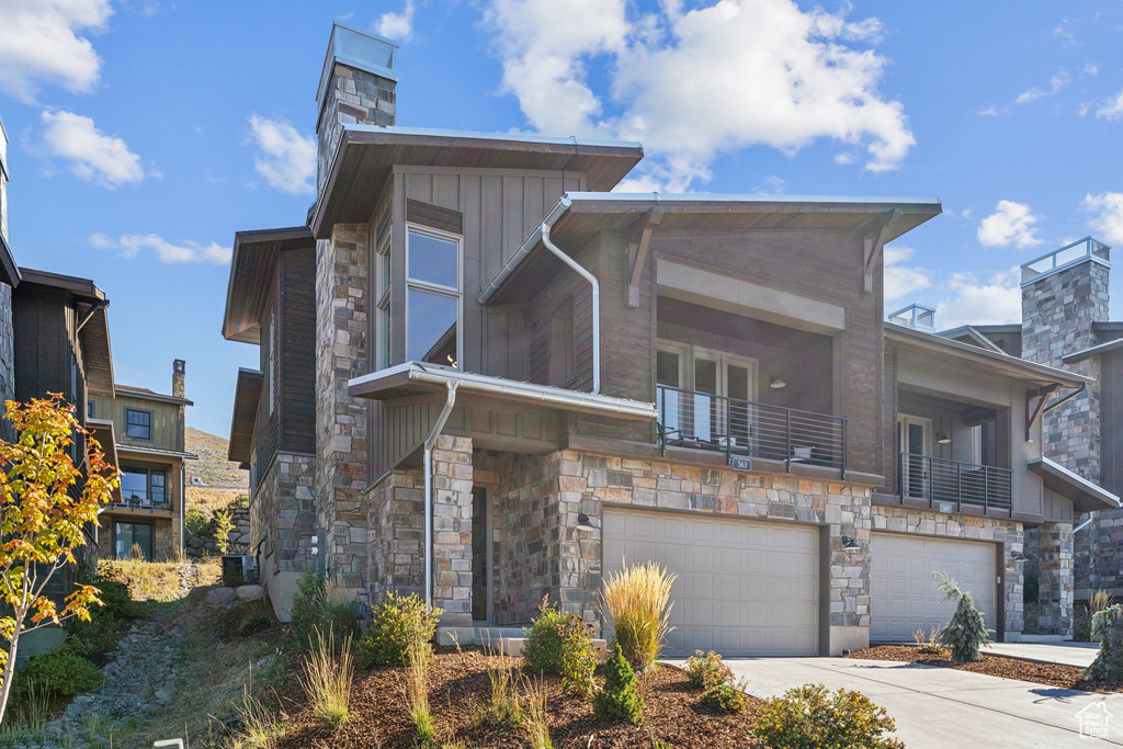 Modern home with stone siding, a garage, a balcony, and concrete driveway