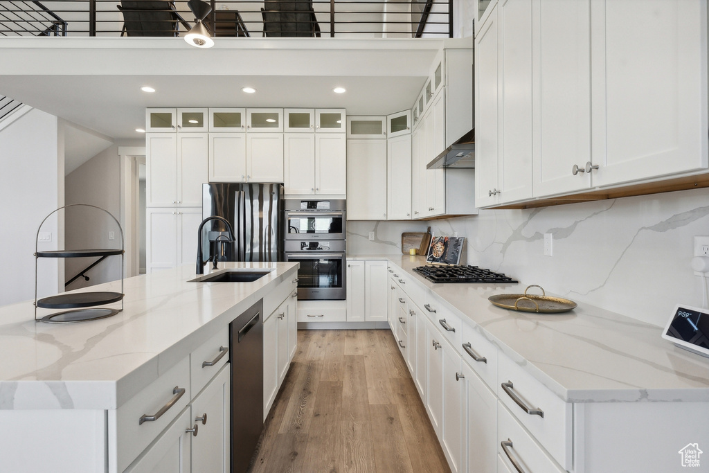 Kitchen featuring white cabinetry, light wood-type flooring, a sink, a large island, and stainless steel double oven