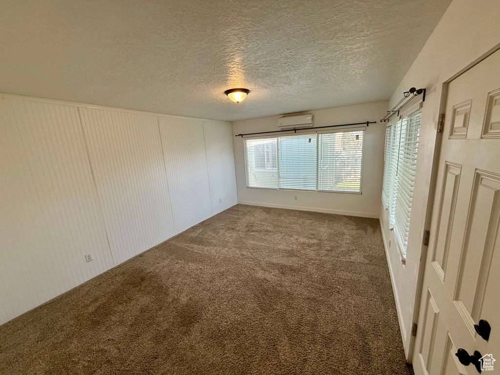 Carpeted spare room featuring an AC wall unit and a textured ceiling