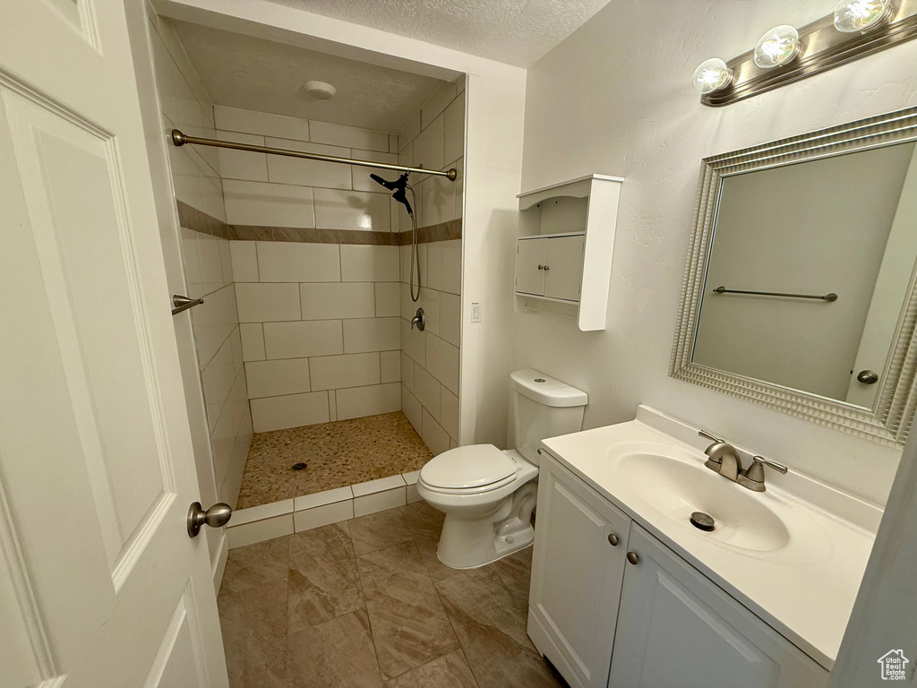 Bathroom with toilet, vanity, a tile shower, and a textured ceiling
