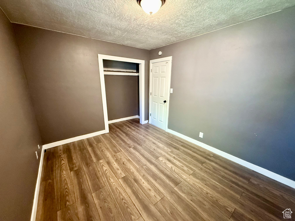 Unfurnished bedroom featuring wood finished floors, baseboards, a closet, and a textured ceiling