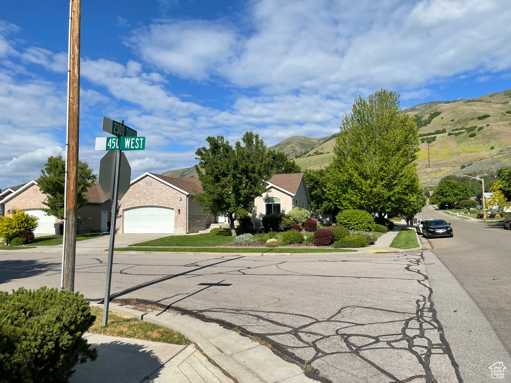 View of asphalt road featuring sidewalks, a mountain view, curbs, traffic signs, and street lights