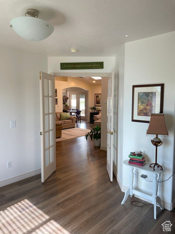 Corridor with french doors, arched walkways, dark wood-style flooring, and baseboards