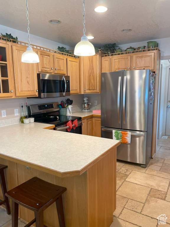 Kitchen featuring appliances with stainless steel finishes, light countertops, a peninsula, stone tile floors, and a breakfast bar