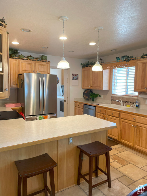 Kitchen featuring appliances with stainless steel finishes, a kitchen breakfast bar, light countertops, a peninsula, and pendant lighting