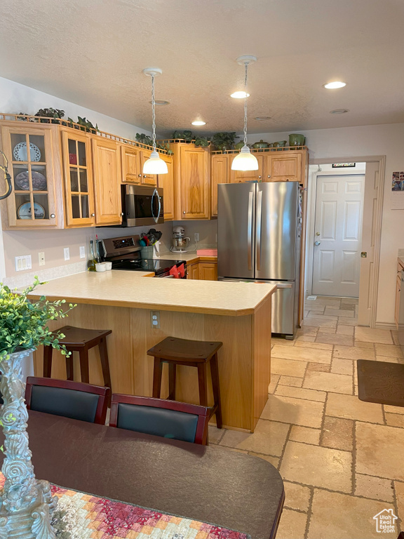 Kitchen featuring appliances with stainless steel finishes, stone tile flooring, a peninsula, light countertops, and glass insert cabinets