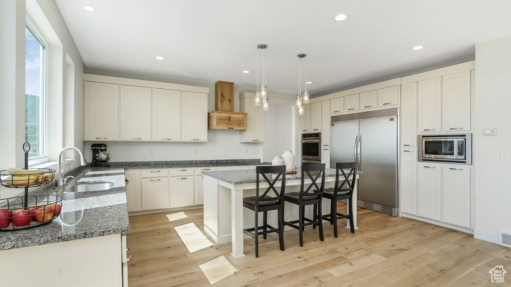 Kitchen with built in appliances, a sink, a breakfast bar, dark stone counters, and a center island
