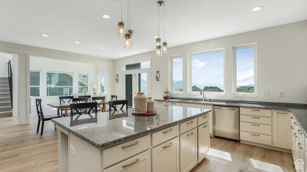 Kitchen with stainless steel dishwasher, light wood finished floors, a center island, dark stone counters, and recessed lighting