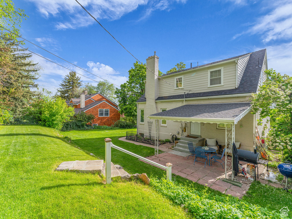 Back of property featuring roof with shingles, a chimney, a yard, and a patio area