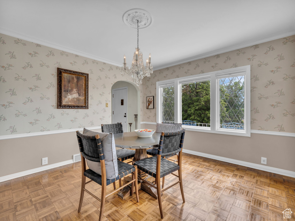 Dining room with arched walkways, a chandelier, baseboards, wallpapered walls, and ornamental molding