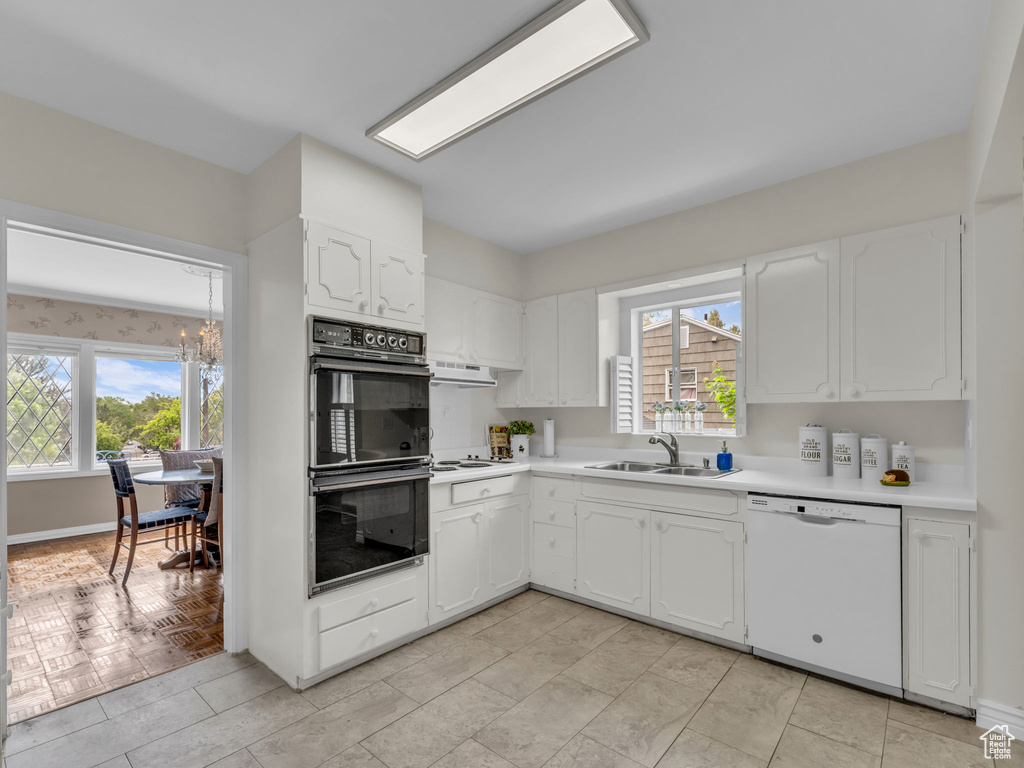 Kitchen featuring white appliances, a sink, a chandelier, white cabinets, and light countertops