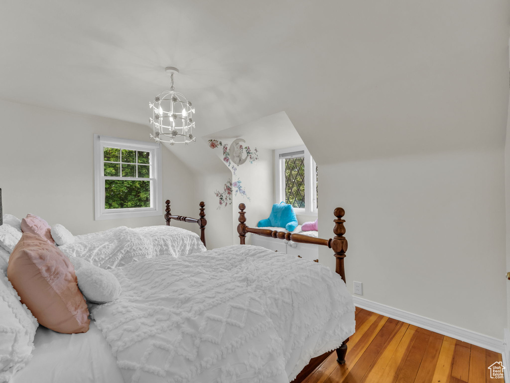 Bedroom featuring wood-type flooring, multiple windows, baseboards, a chandelier, and vaulted ceiling