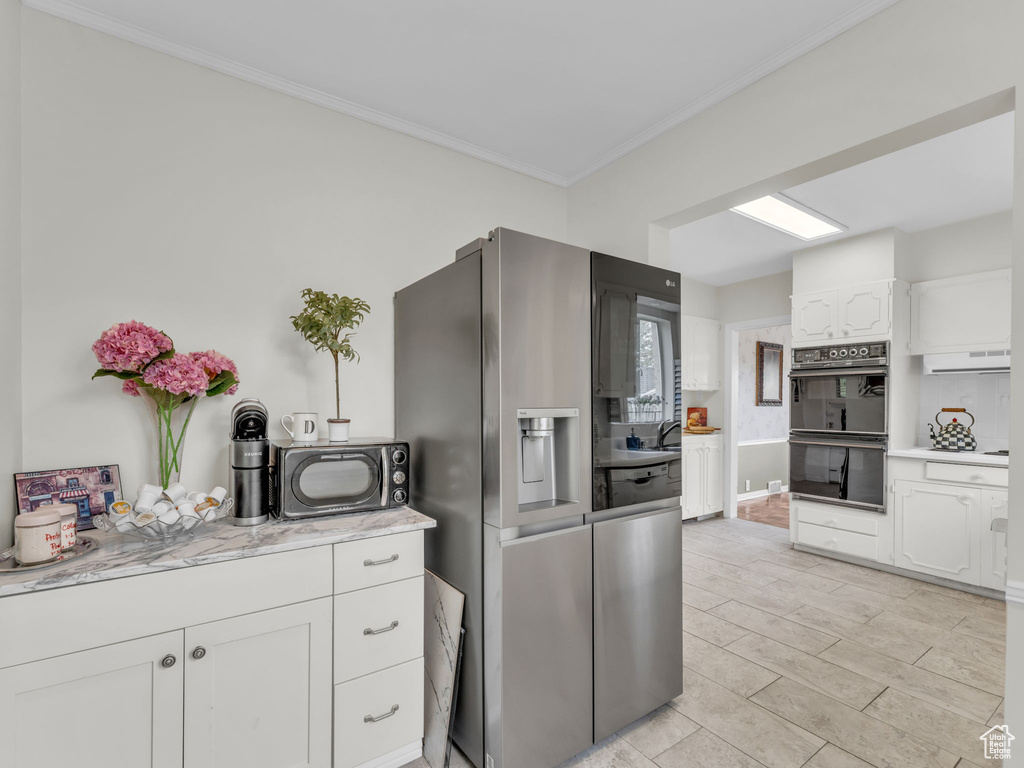 Kitchen featuring stainless steel refrigerator with ice dispenser, white cabinets, crown molding, and exhaust hood